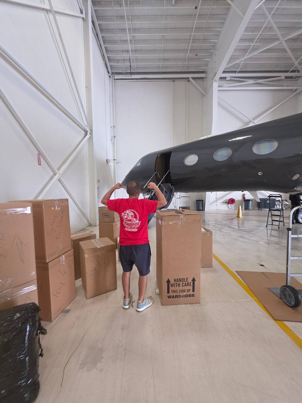 Apache Moving crew member wrapping boxes beside a private jet in a South Florida hangar