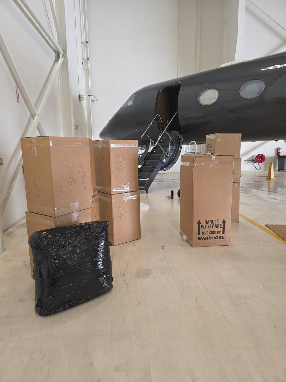 Fragile and wardrobe moving boxes staged near a private jet's boarding stairs